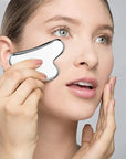 Woman using stainless steel gua sha on face to relieve puffiness and tension