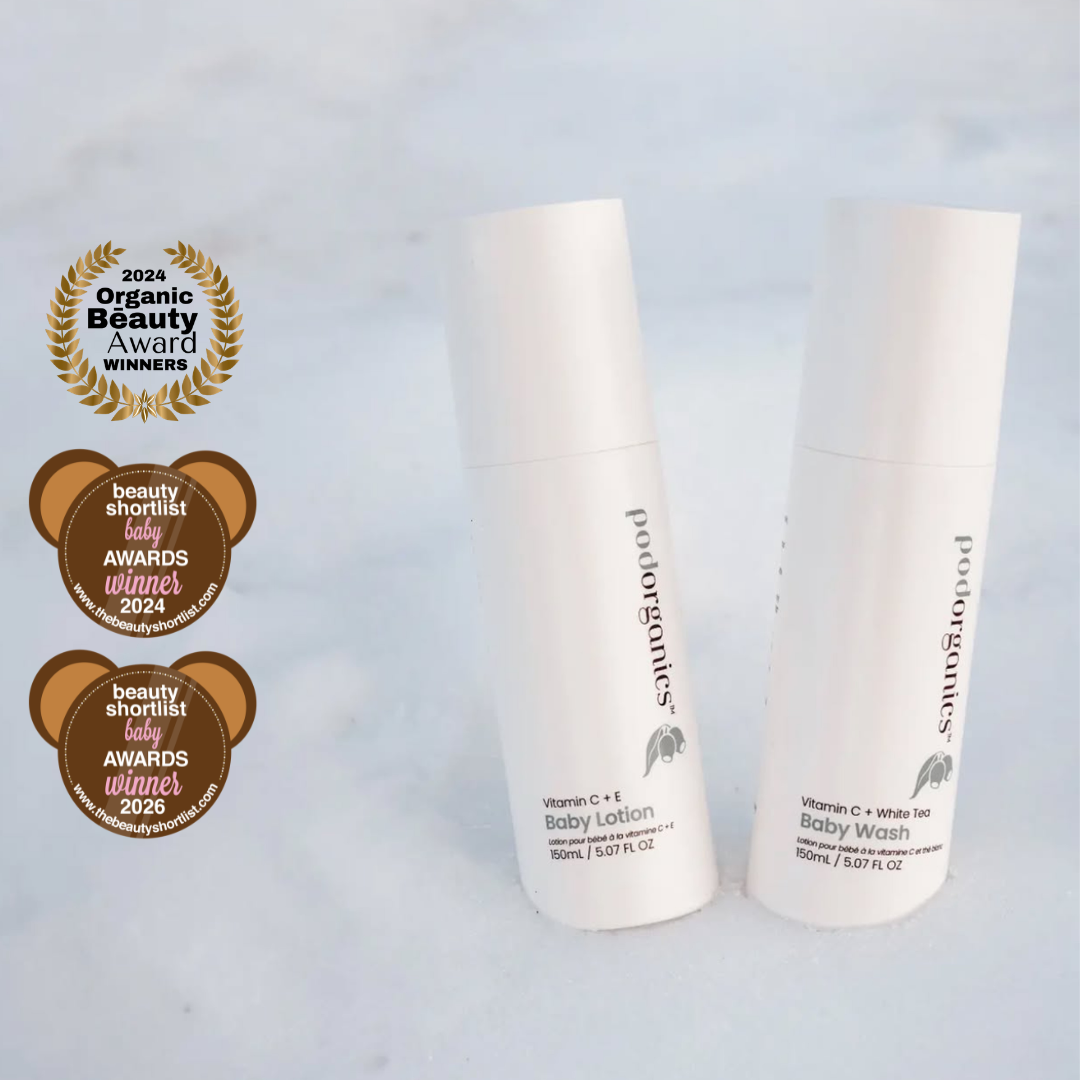 Two white Podorganics baby care tubes standing upright on a light marble-like surface, with three award badges displayed to the left. The tubes are labeled 'podorganics' and include Baby Lotion and Baby Wash variants.